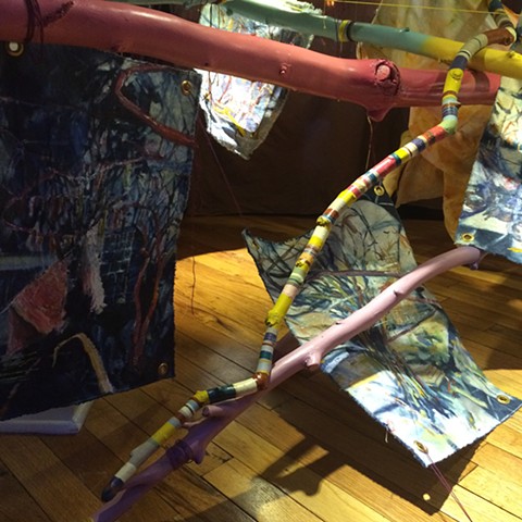 Brightly painted sticks crossing each other, providing hanging system for unstretched oil paintings on indigo dyed canvas, all installed in the back space of a 1991 Ford Bronco