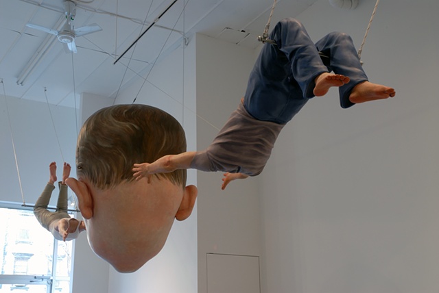 Polychrome figurative sculpture of a life-size headless woman and man tossing a huge child's head between them on a trapeze