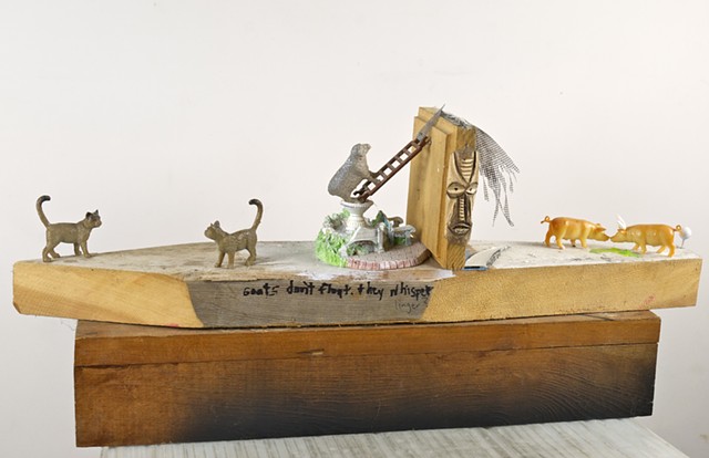 Linger is a Modern Assemblage Art piece using found objects and barn animals along with a voodoo mask, written word, and fencing to create a barnyard scene with cats, goats, sheep, pigs, and horns.